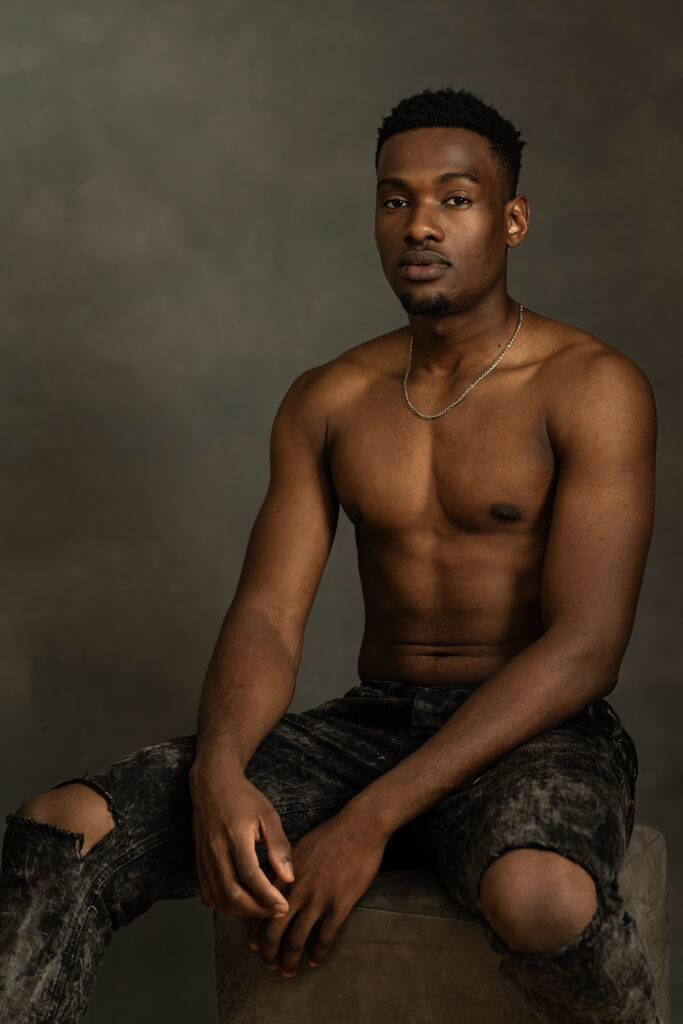 Studio portrait of a male model seated against a dark textured backdrop