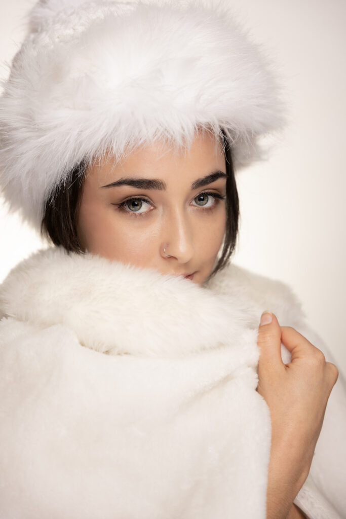 Model wearing a white faux-fur hat and wrap in a styled fashion product photograph