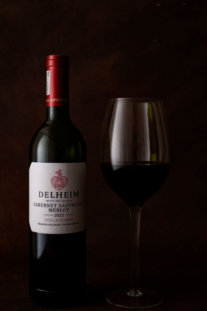 Delheim Cabernet Sauvignon Merlot bottle with a glass of red wine in a styled product photograph